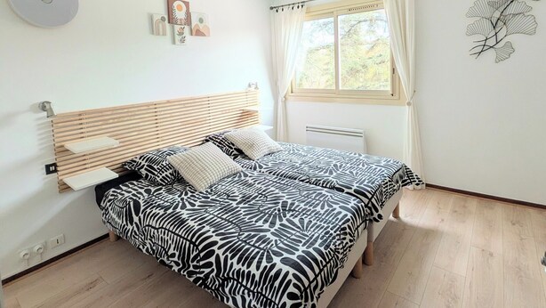 Ein Schlafzimmer mit Bett, einem Fenster mit Vorhängen, einer Wandleuchte und einem Heizkörper.