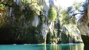 Ein Boot auf ruhigem, türkisfarbenem Wasser, umgeben von felsigen Klippen mit dichtem Grün.