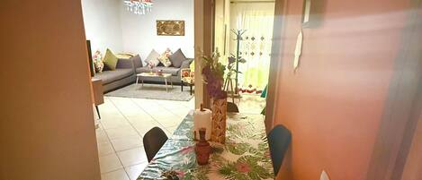 A dining area with a table set for two, a sofa in the background, and a doorway leading to another room.