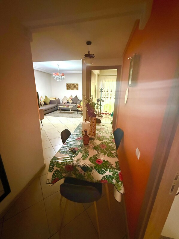 A dining area with a table set for two, a sofa in the background, and a doorway leading to another room.