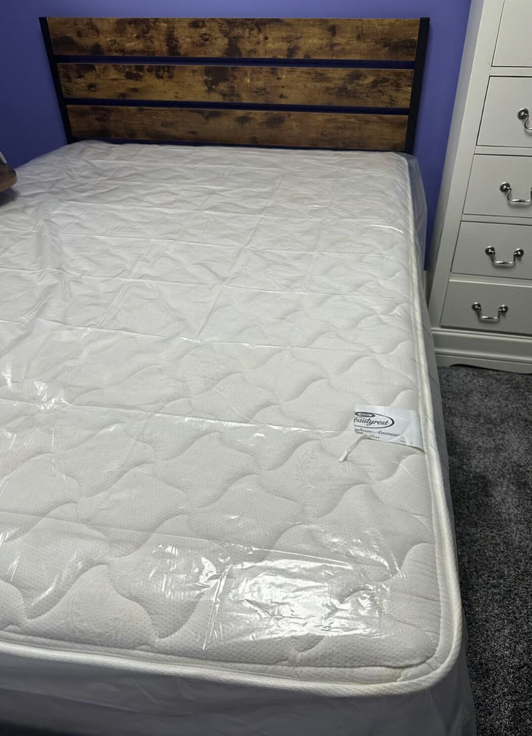 A bed with a wooden headboard, a mattress, and a white dresser with drawers.