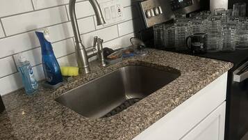 A kitchen with a granite countertop, stainless steel sink, and a black stove.