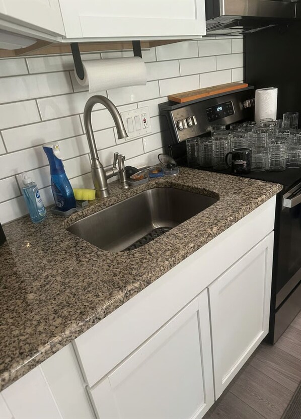 A kitchen with a granite countertop, stainless steel sink, and a black stove.