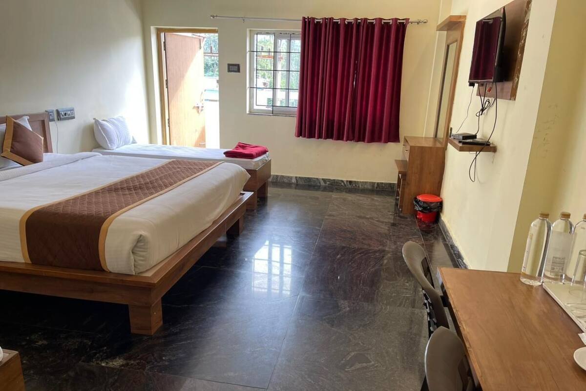 Una habitación de hotel con una cama grande, un escritorio de madera, un televisor y un ventanal con cortinas.