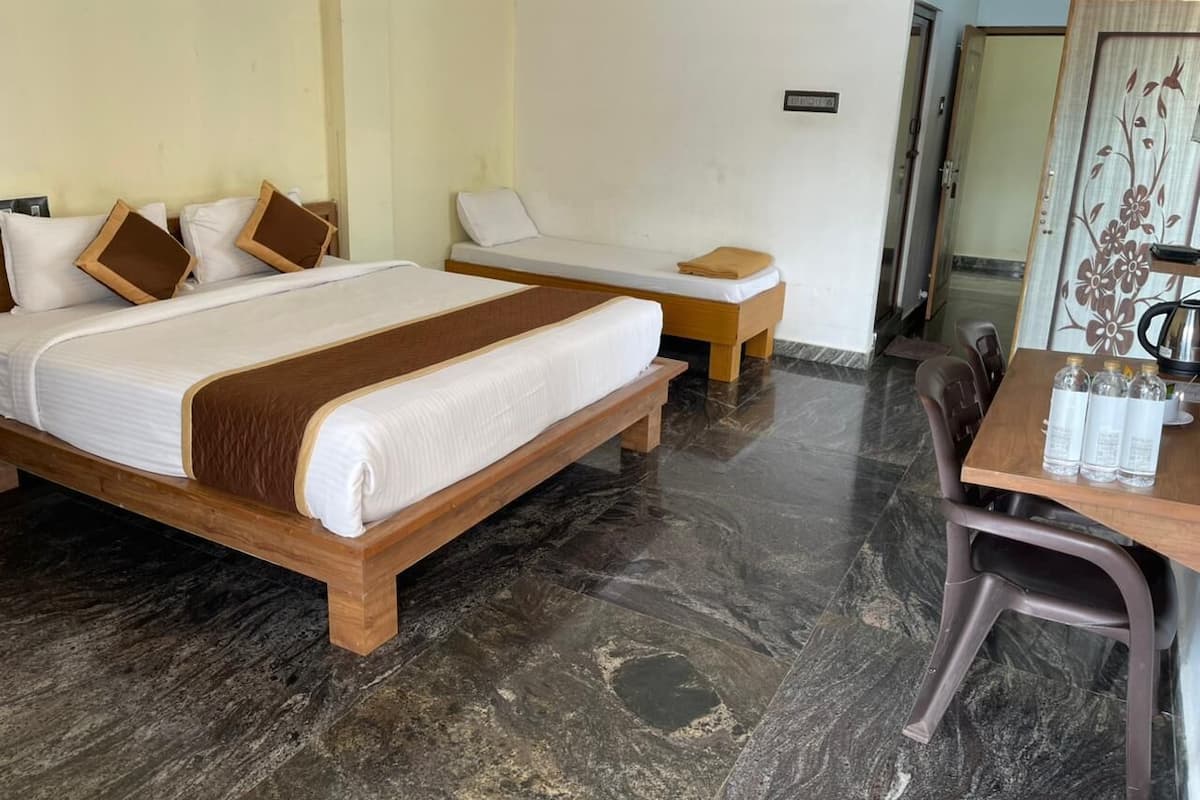 Una habitación de hotel con dos camas, una mesa de madera con sillas y una mesita con botellas.