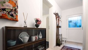A hallway with a wooden console table displaying dishes and a vase of flowers. A large floral tapestry hangs on the wall, and a giraffe sculpture is mounted on the wall. - Charming Apartment with Private Access at Thoeny (Utting am Ammersee)