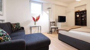 A modern bedroom with a bed, a sofa, a TV, and a small table with a vase. - Charming Apartment with Private Access at Thoeny (Utting am Ammersee)