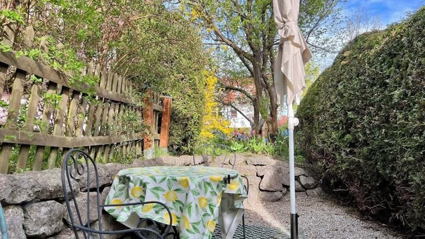 A garden patio with a table and chairs, surrounded by stone walls and a wooden fence. - Charming Apartment with Private Access at Thoeny (Utting am Ammersee)
