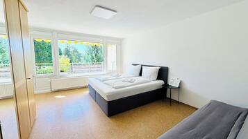 Ein Schlafzimmer mit Bett, Nachttisch, Heizkörper und einem Fenster mit Blick ins Grüne.