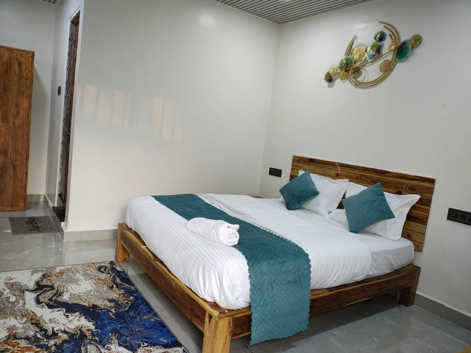Una cama bien hecha con ropa de cama blanca y detalles azul verdoso, un cabecero de madera y un elemento decorativo en la pared.