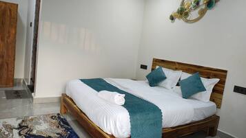 Una cama bien hecha con ropa de cama blanca y detalles azul verdoso, un cabecero de madera y un elemento decorativo en la pared.