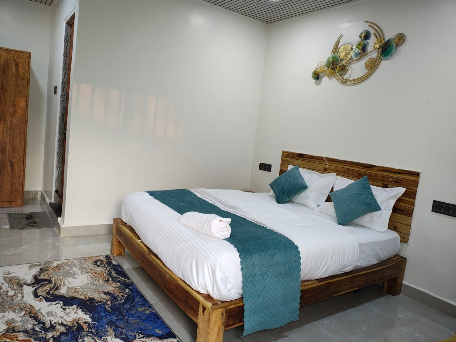 A bedroom with a wooden bed, white bedding, teal throw, and a decorative wall piece.