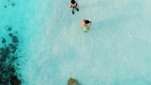 An aerial view of a beach with clear turquoise water, a large rock formation, and two people swimming. - Endorphins Beach Villa (Dhiffushi)
