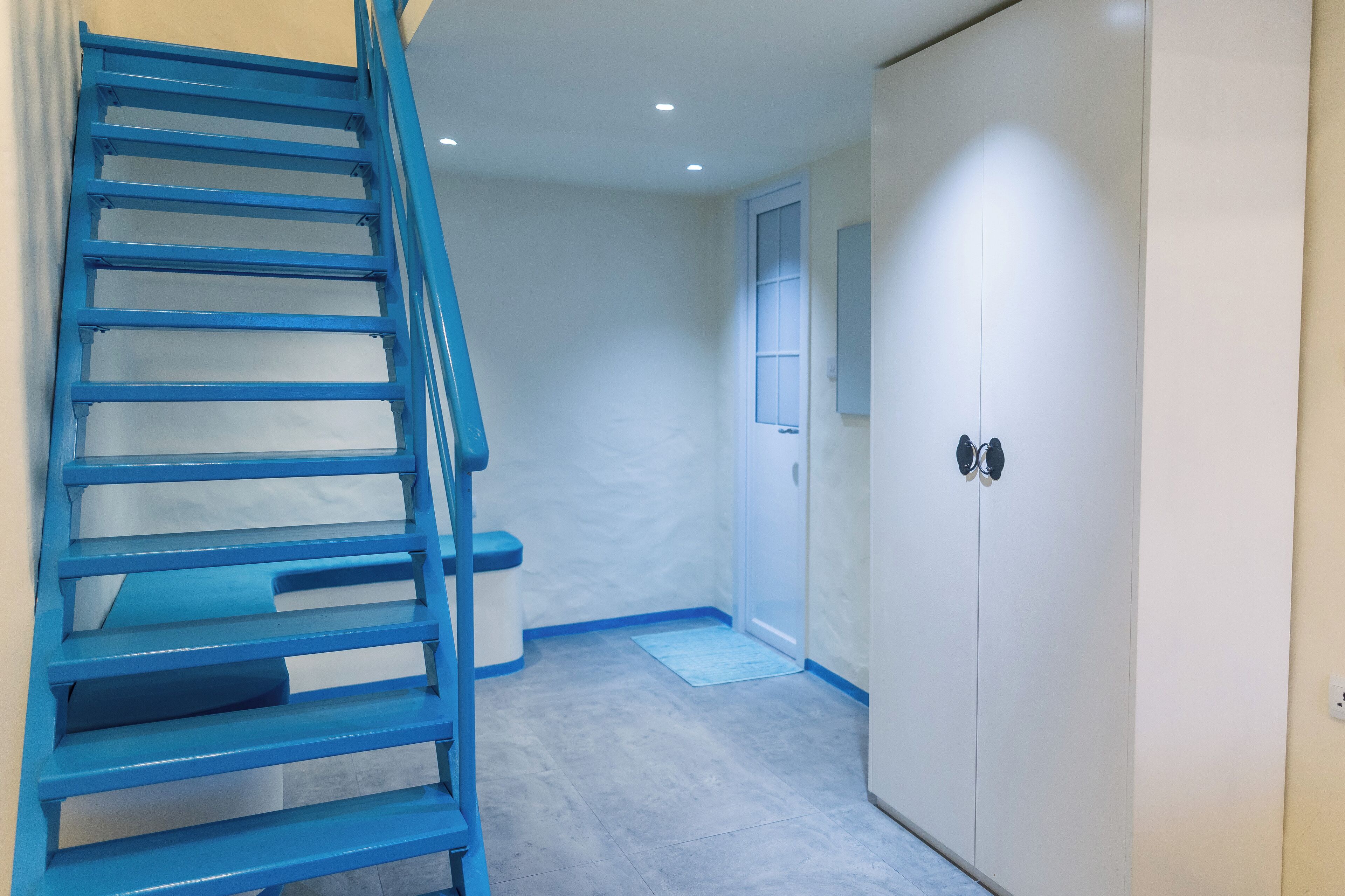 A staircase leading to a door, a door with a shoe rack, and a light-colored floor.
