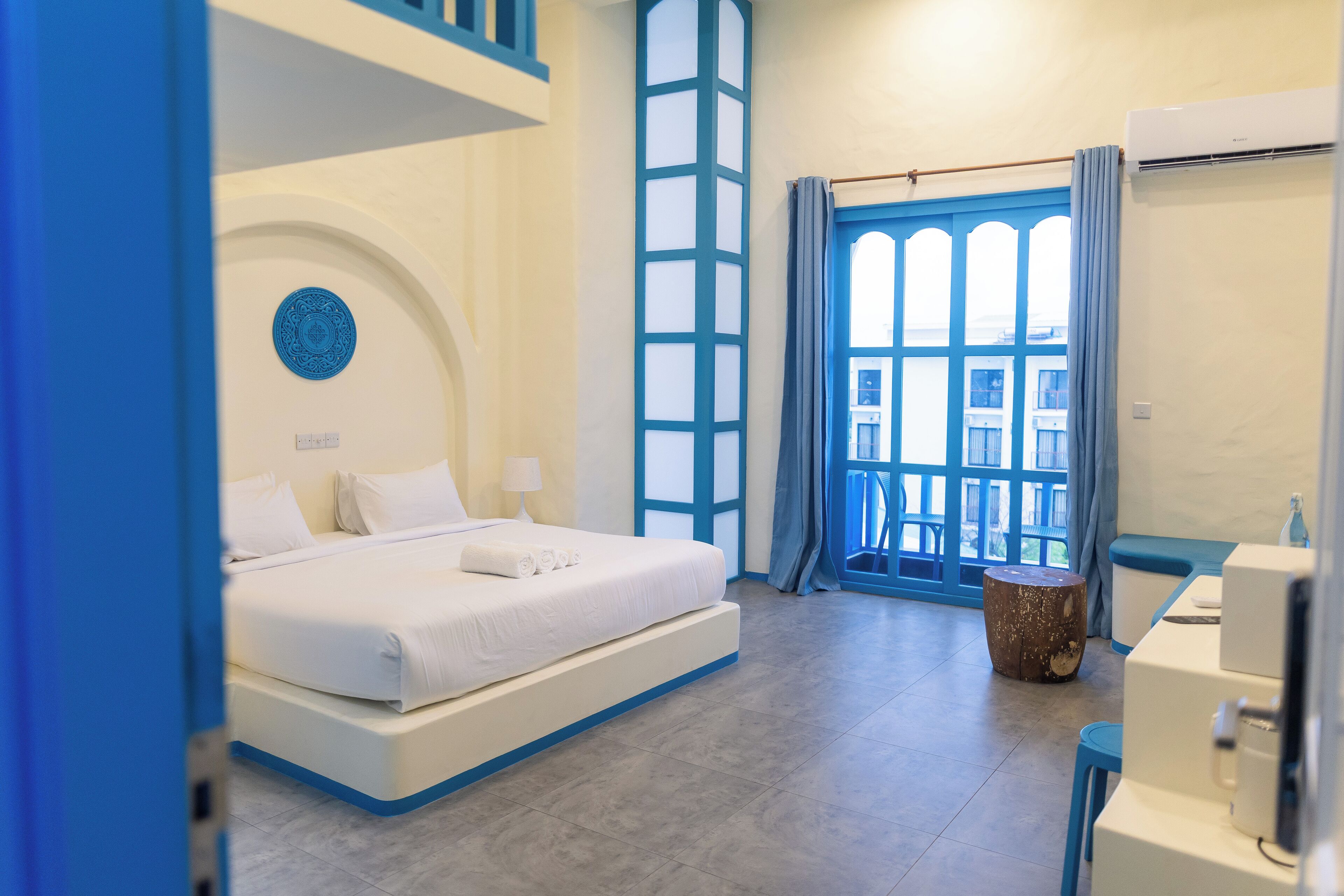 A modern hotel room with a large bed, a small round table, and a view of the city through a large window.