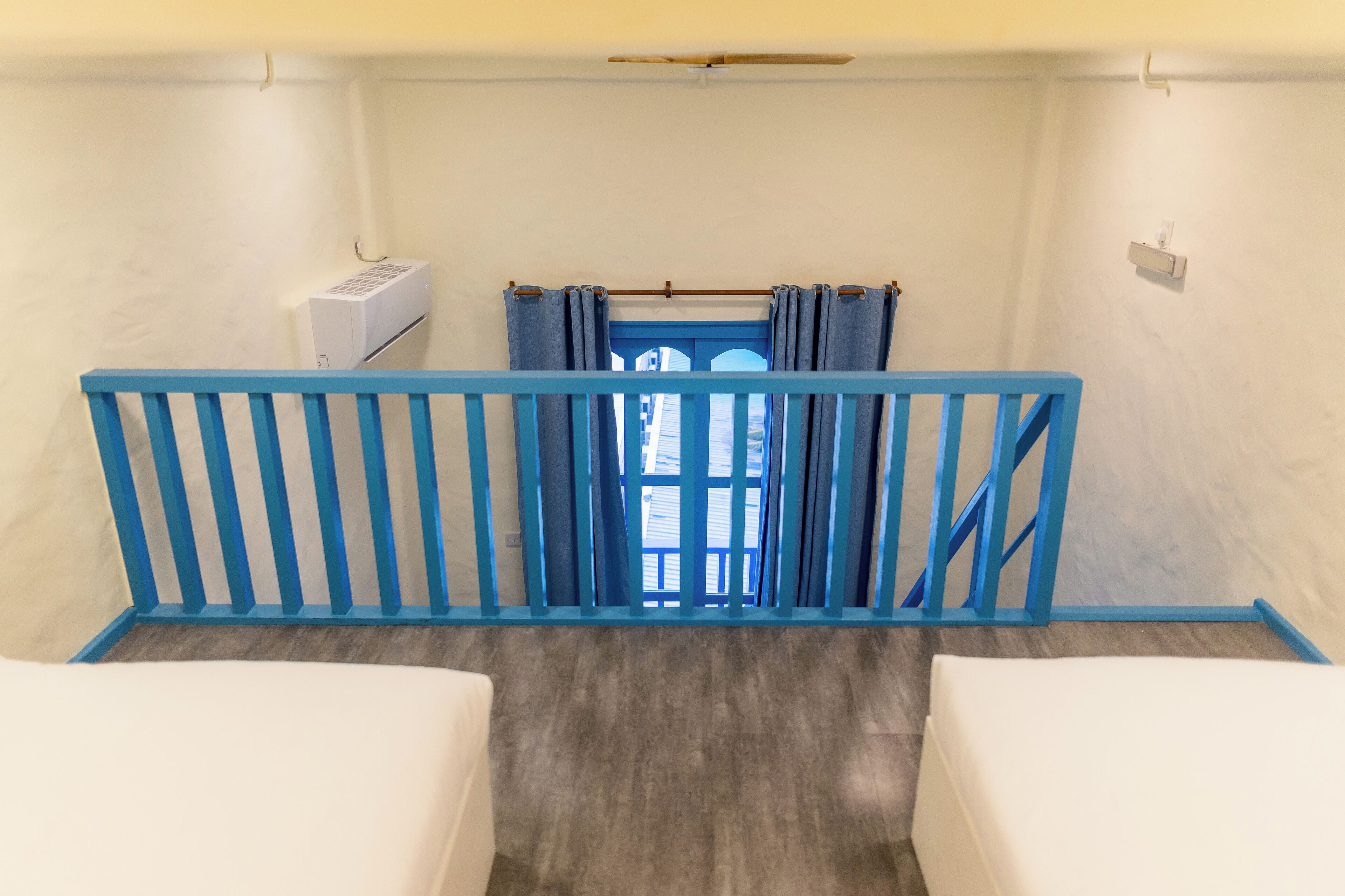 A room with a blue railing, a window with curtains, and a white air conditioning unit.