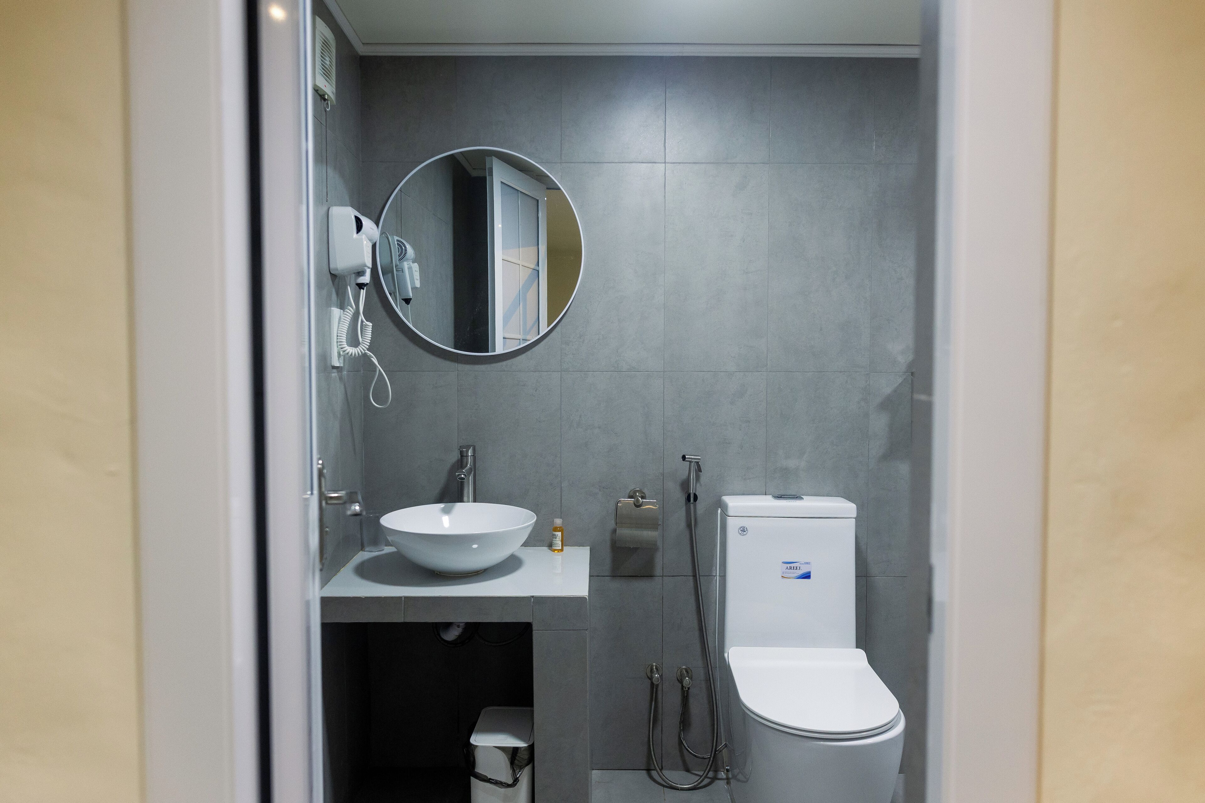 A modern bathroom with a white sink, a round mirror, a toilet, and a handheld showerhead.