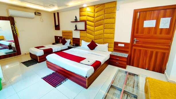 A hotel room with a large bed, two bedside tables, a mirror, and a wooden door with a sign. - Hotel Royal Aanandam (Gwalior)