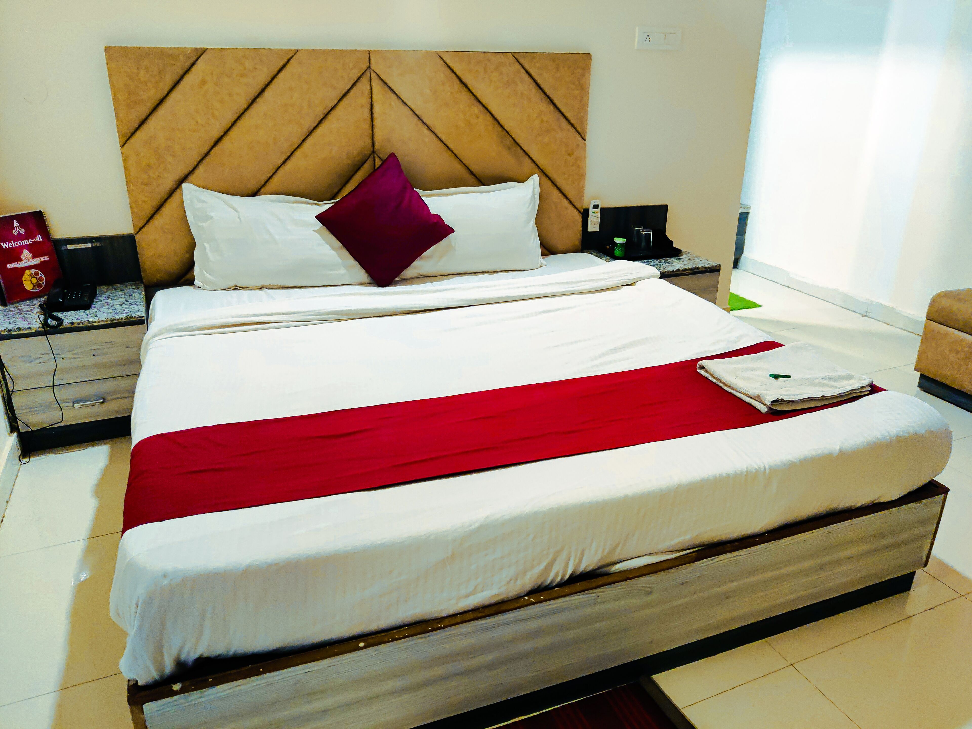 A neatly made bed with a red blanket, a wooden headboard, and a white pillow.