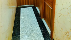 A narrow hallway with wooden doors, a marble floor, and a light switch on the wall. - Hotel Royal Aanandam (Gwalior)
