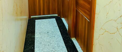 A narrow hallway with wooden doors, a marble floor, and a light switch on the wall.