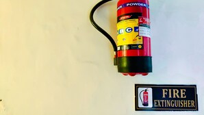 A fire extinguisher mounted on a wall with a sign below it that reads "FIRE EXTINGUISHER". - Hotel Royal Aanandam (Gwalior)