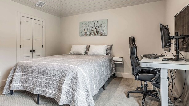 A bedroom with a bed, a desk with a computer, and a chair.
