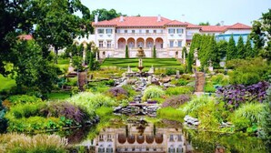 A large, classical building with a symmetrical facade, a central fountain, and a well-maintained garden with a pond.