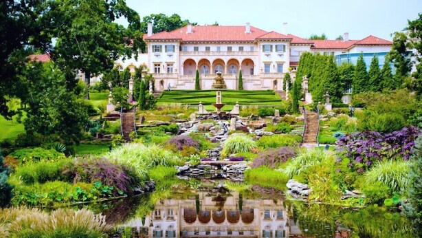 Een groot, klassiek gebouw met een symmetrische gevel, een centrale fontein en een goed onderhouden tuin met een vijver.