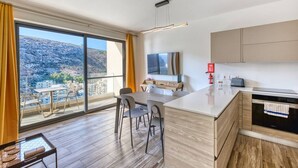A modern kitchen with a large island, a dining area with a view, and a flat-screen TV mounted on the wall. - Stylish Apartment - Breathtaking Views in Xlendi (Munxar)