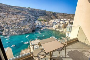 A balcony with a table and chairs overlooking a coastal town with boats in the water. - Stylish Apartment - Breathtaking Views in Xlendi (Munxar)