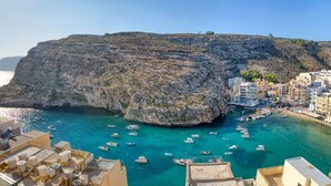 A coastal town with rocky cliffs, clear turquoise waters, and numerous boats anchored near the shore. - Stylish Apartment - Breathtaking Views in Xlendi (Munxar)