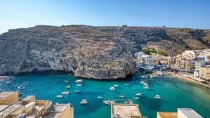A coastal town with a rocky cliff, clear turquoise waters, and numerous boats docked at the marina. - Stylish Apartment - Breathtaking Views in Xlendi (Munxar)