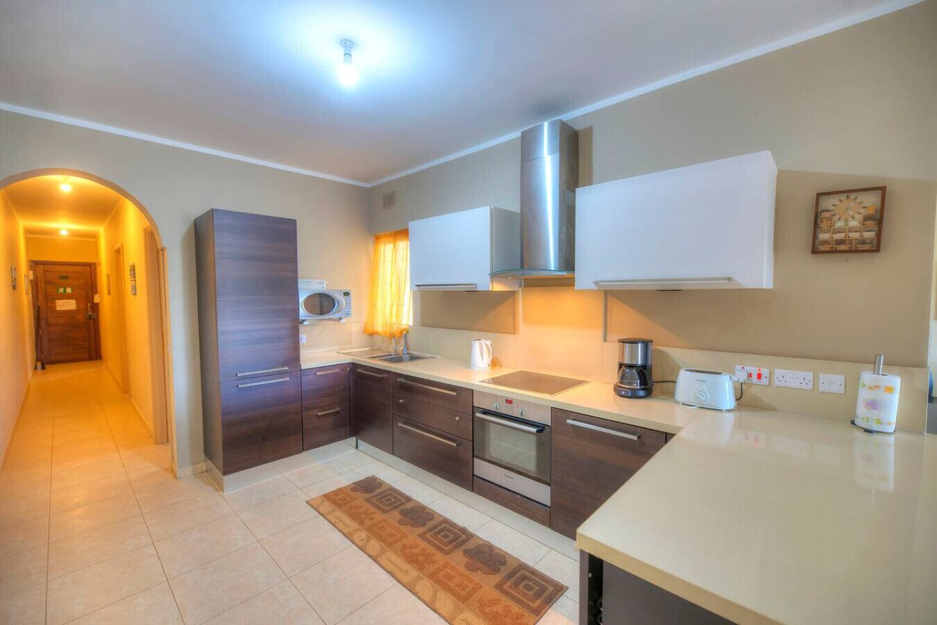 A modern kitchen with dark wooden cabinets, a stainless steel range hood, a microwave, and a coffee maker.