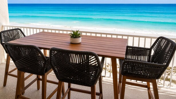 A wooden table with four wicker chairs, a potted plant, and a view of a beach with clear blue water and a white sandy shore. - Renovated 2 Bed, 2 Bath, Beachfront w/ Gulf views (Longboat Key)