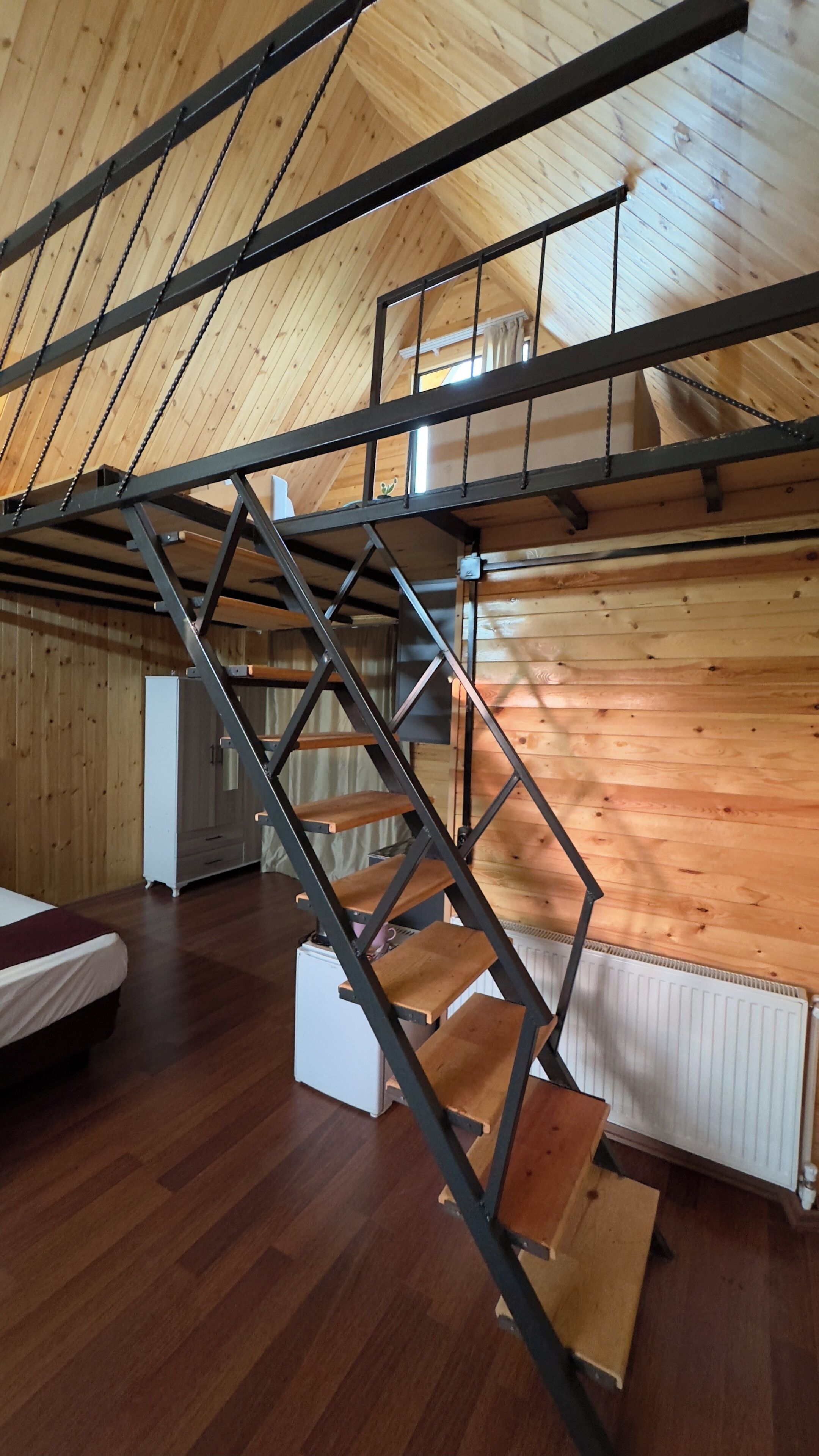Un espai tipus loft amb una escala metàl·lica, bigues de fusta i un radiador blanc.
