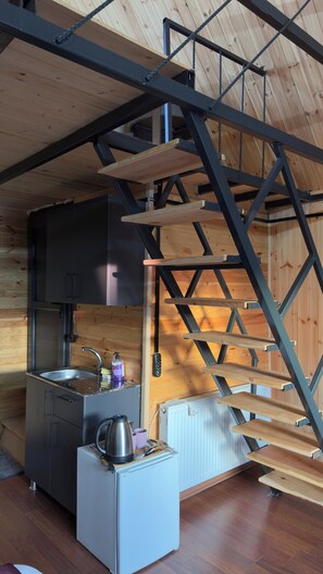 A compact kitchen with a sink, cabinets, and a small refrigerator. A wooden ladder and a white radiator are also visible. - TERAS GARDEN BUNGALOV HATAY (Altınözü)