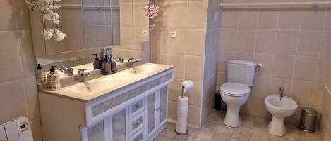 A modern bathroom with a large mirror, two sinks, a toilet, and a bidet.