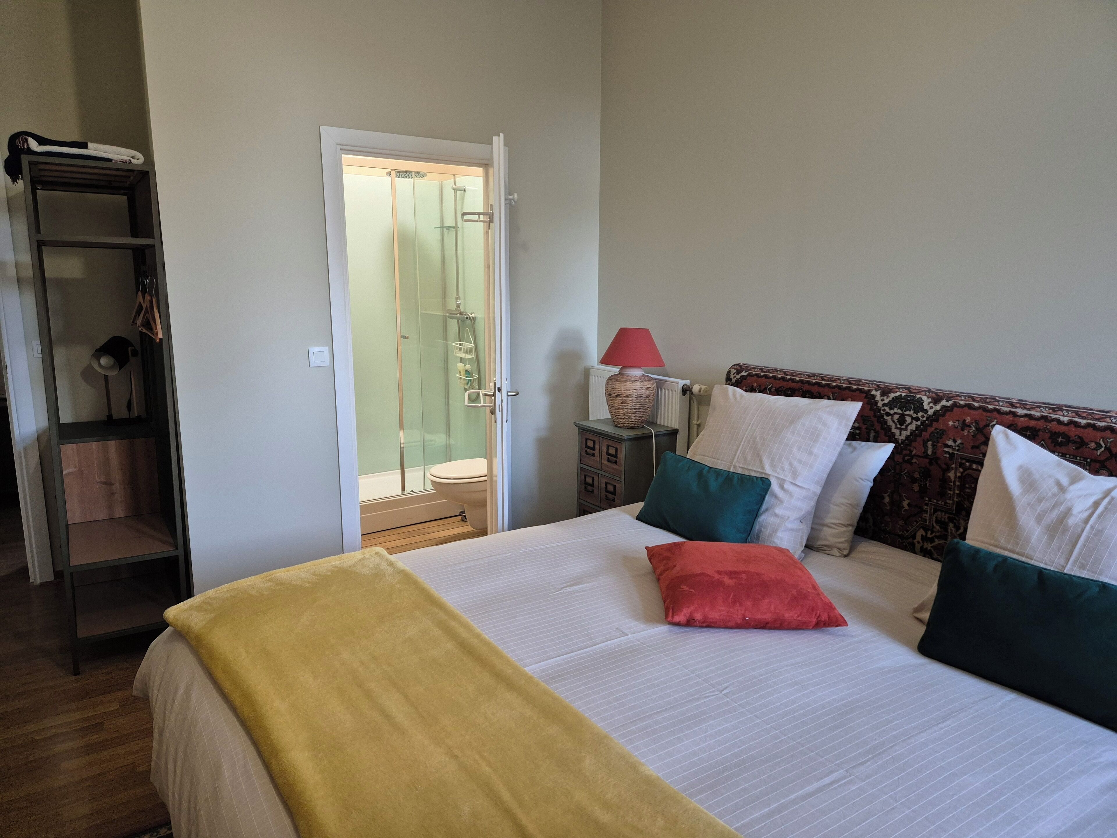 Un dormitorio con cama, mesita de noche, lámpara y vista al baño.