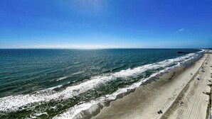 A beach with a long stretch of sand, waves crashing onto the shore, and a clear blue sky. - Atalaya Tower 1603 - Three Bedroom, Oceanfront Condo in Garden City Beach (Garden City Beach)