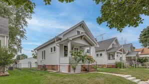 A single-story house with a front porch, a small front yard, and a visible garage. - Fresh Coast Craftsman - Pet Friendly | Near Lake (Sheboygan)