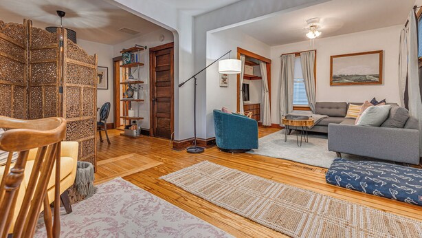 A spacious living room with wooden flooring, a sofa, a blue armchair, and a dining area with a wooden table and chairs. - Fresh Coast Craftsman - Pet Friendly | Near Lake (Sheboygan)