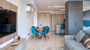 A modern living room with a grey sofa, a wooden console table, and a dining area with blue chairs and a small table. - City Centre St. Julian's 1BR Apartment - 4 Guests (Saint Julian's)