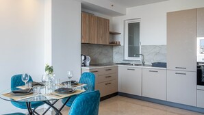 A modern kitchen with white cabinets, a marble backsplash, and a dining area with a glass table and blue chairs. - Top Location Penthouse in St. Julian's - 4 Guests (Saint Julian's)