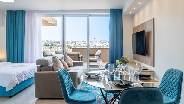 A modern hotel room with a balcony, a sofa, a dining table set for two, and a TV mounted on the wall. - Top Location Penthouse in St. Julian's - 4 Guests (Saint Julian's)