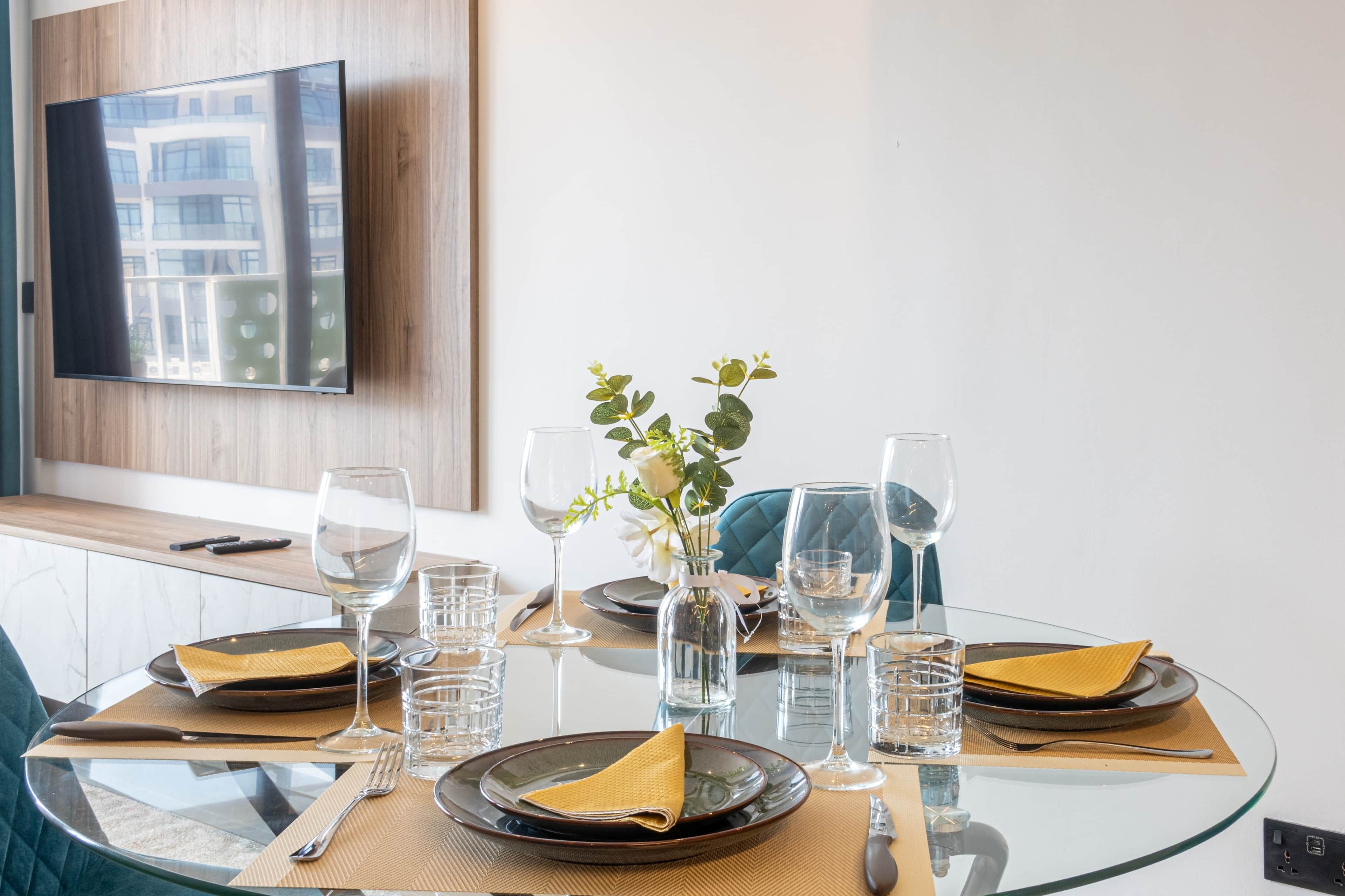 A dining table set with plates, cutlery, glasses, and a vase with flowers.