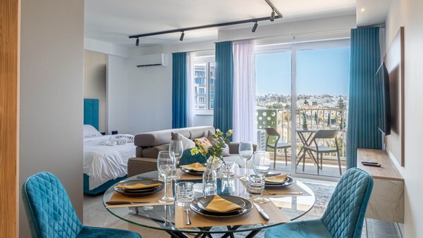 Een moderne hotelkamer met een eethoek, een bed en een balkon met uitzicht op de stad.