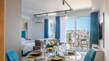 A modern hotel room with a dining area, a bed, and a balcony with a city view.