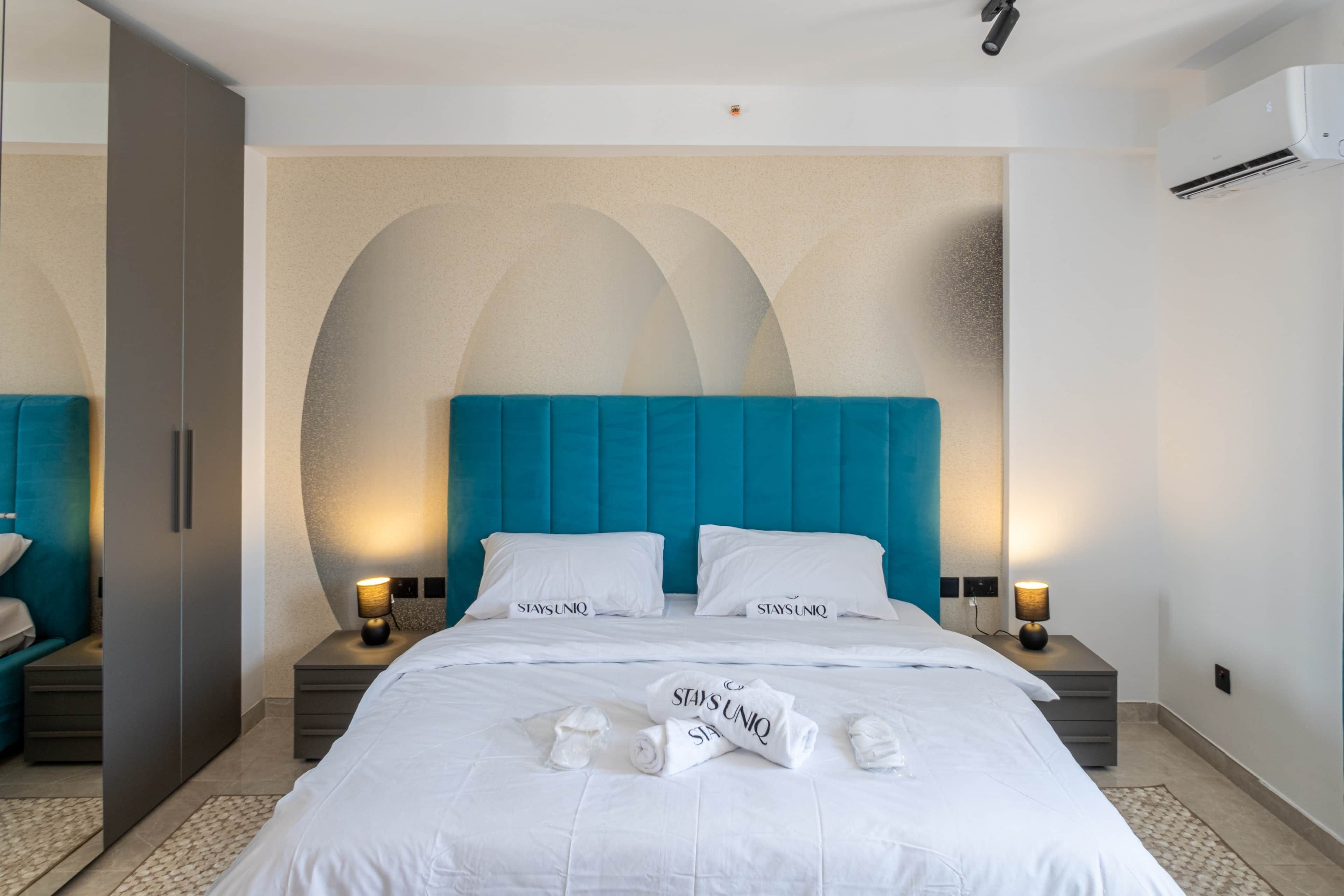 A hotel room with a large bed, two bedside tables, a wardrobe, and a wall with a geometric design.