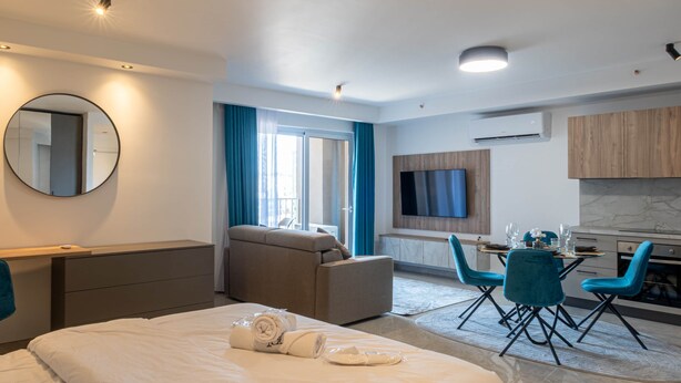 Una habitació d'hotel moderna amb un llit, un sofà, una zona de menjador amb cadires, una televisió i una cuina.